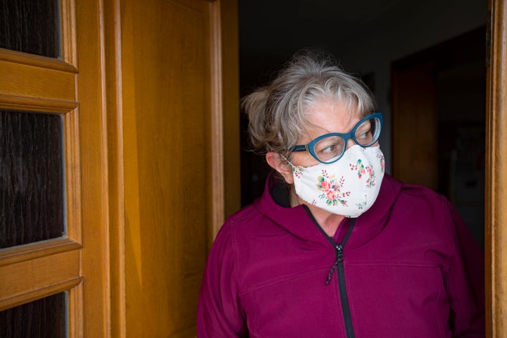 In this stock photo, a woman in a face-mask leans out her front door. Home-buying is changing in the pandemic, with virtual tours and "COVID clauses" now common.