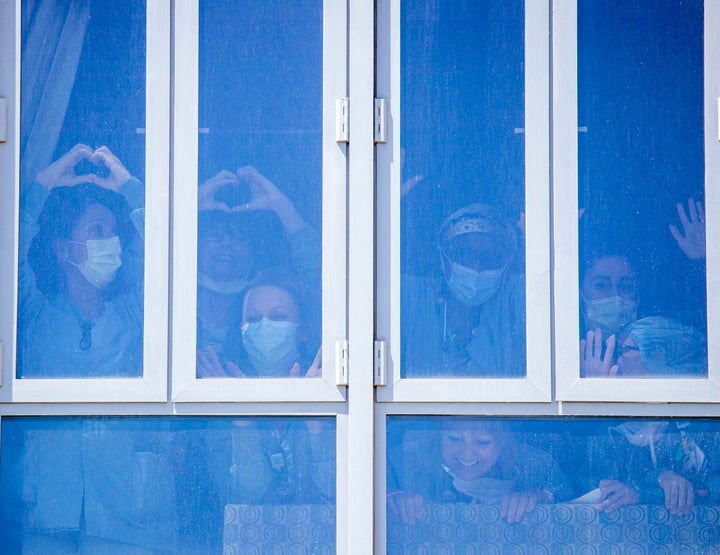 UC Irvine Medical Center health care workers bang on the windows in a return of gratitude as they watch Orange County first responder vehicles participate in a drive-by parade to show support for them on April 14, 2020.
