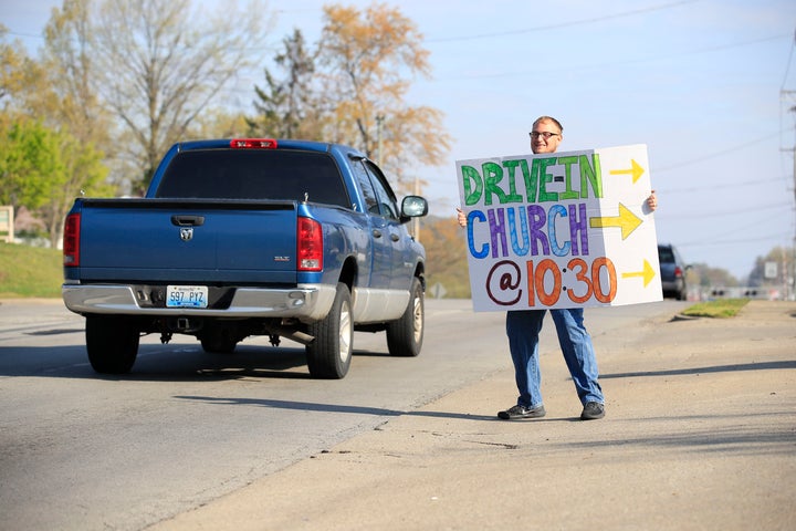 A worshipper holds a sign to alert drivers to a drive-in service at On Fire Christian Church on April 5, 2020, in Louisville, Kentucky.