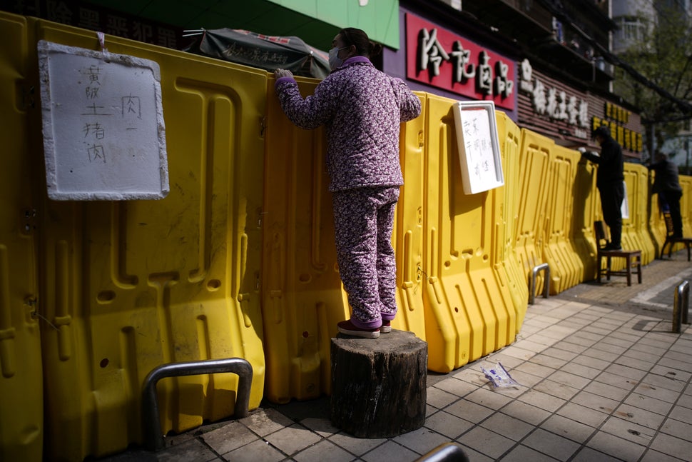 Residents pay for groceries by standing on chairs to peer over barriers set up by a wet market on a street in Wuhan, the epic