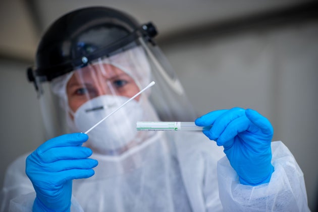 A health care worker in Germany tests a patient for coronavirus at a drive-thru testing center on April