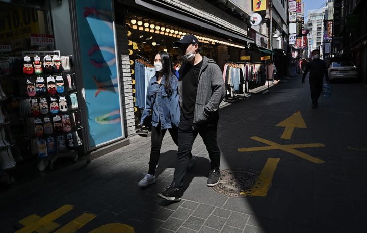 A couple wearing face masks walk through a shopping district in Seoul on April 23, 2020.