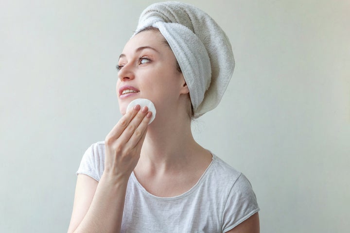 Beauty portrait of smiling woman in towel on head with soft healthy skin removing make up with cotton pad isolated on white background. Skincare cleansing spa relax concept