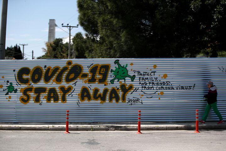 A woman walks in front of graffiti against coronavirus, written by soccer fans near the under construction stadium of the AEK soccer club in Athens, Wednesday, April 8, 2020. The COVID-19 causes mild or moderate symptoms for most people, but for some, especially older adults and people with existing health problems, it can cause more severe illness or death. (AP Photo/Thanassis Stavrakis)