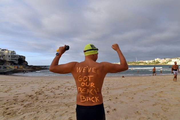 A man poses with a message on his back before enjoying his first swim after Bondi Beach reopened following a five week closure in Sydney on April 28, 2020, amid the novel coronavirus pandemic. - Swimmers and surfers returned to Sydney's famed Bondi Beach almost six weeks after it was closed amid a spike in coronavirus cases. (Photo by Saeed KHAN / AFP) (Photo by SAEED KHAN/AFP via Getty Images)