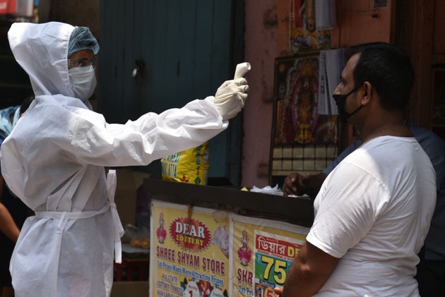 A municipal health department worker screens people for body temperature at Poddar Court area in Kolkata...