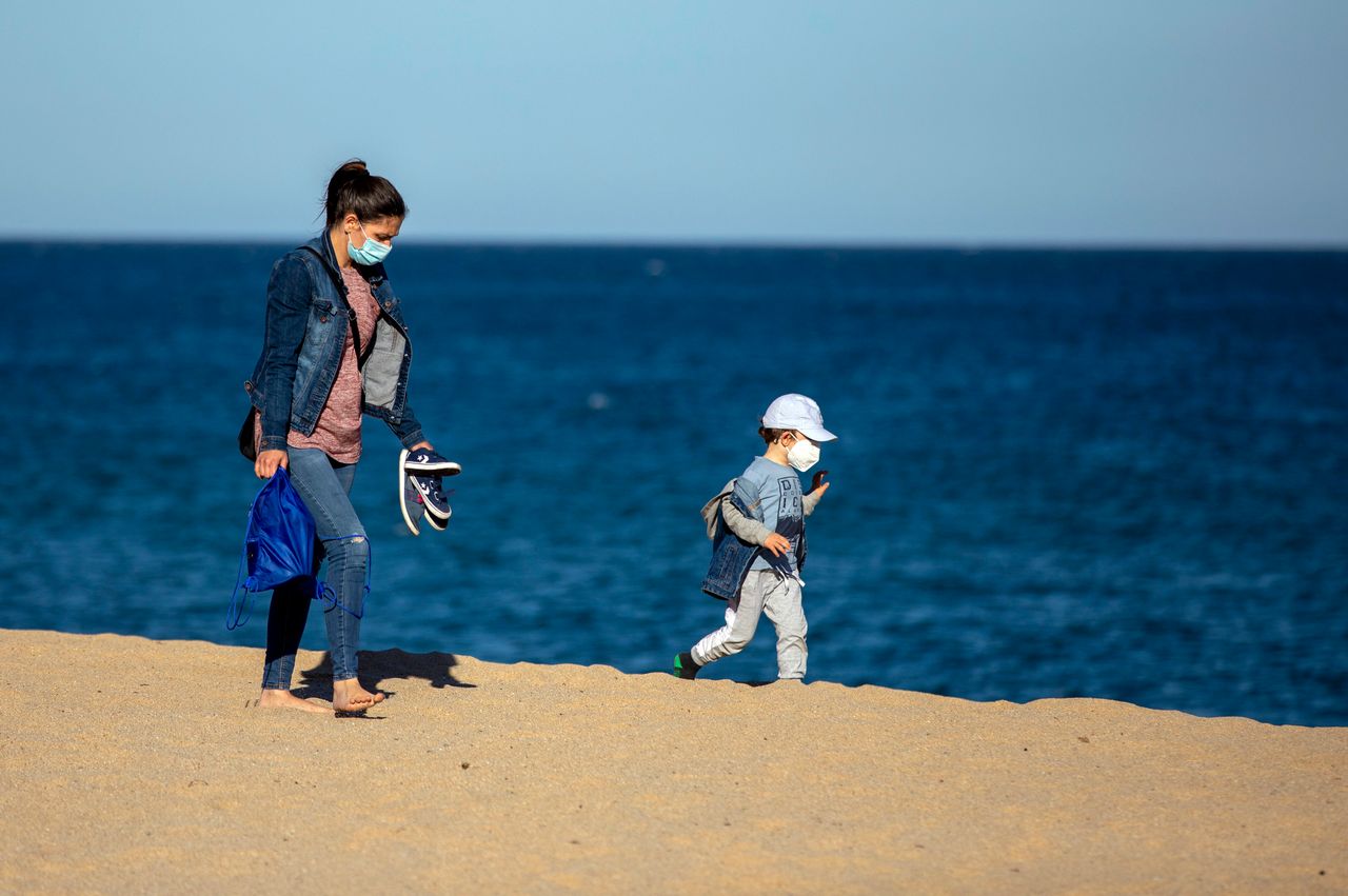 A woman and her son wear face masks as they walk on a beach in Badalona, near Barcelona