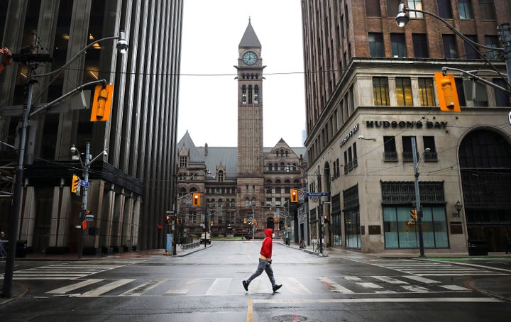 A man runs across an empty intersection in Toronto. After weeks of practicing social distancing, Canadians are wondering when life will return to normal. 