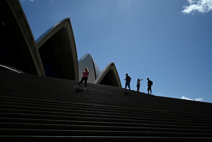 A handful of tourists stand atop the mostly deserted steps of the Sydney Opera House, where scheduled public performances hav