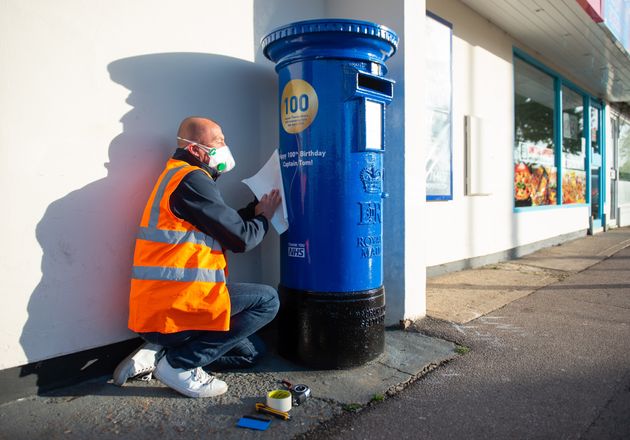 A man preopares a letter box painted blue to mark the 100th birthday of Second World War veteran Captain Tom Moore close to the home in Marston Moretaine, near Bedford.