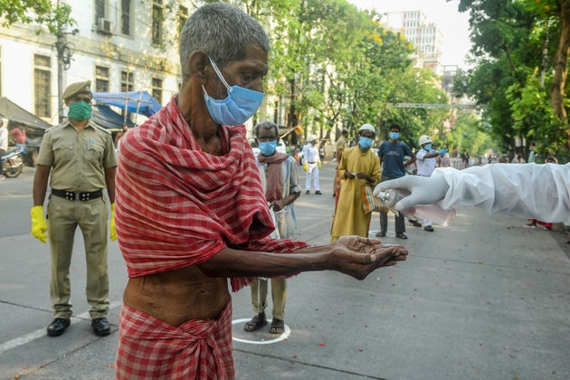 A slum dweller in Kolkata cleans his hands with sanitizer before collecting relief material on April...