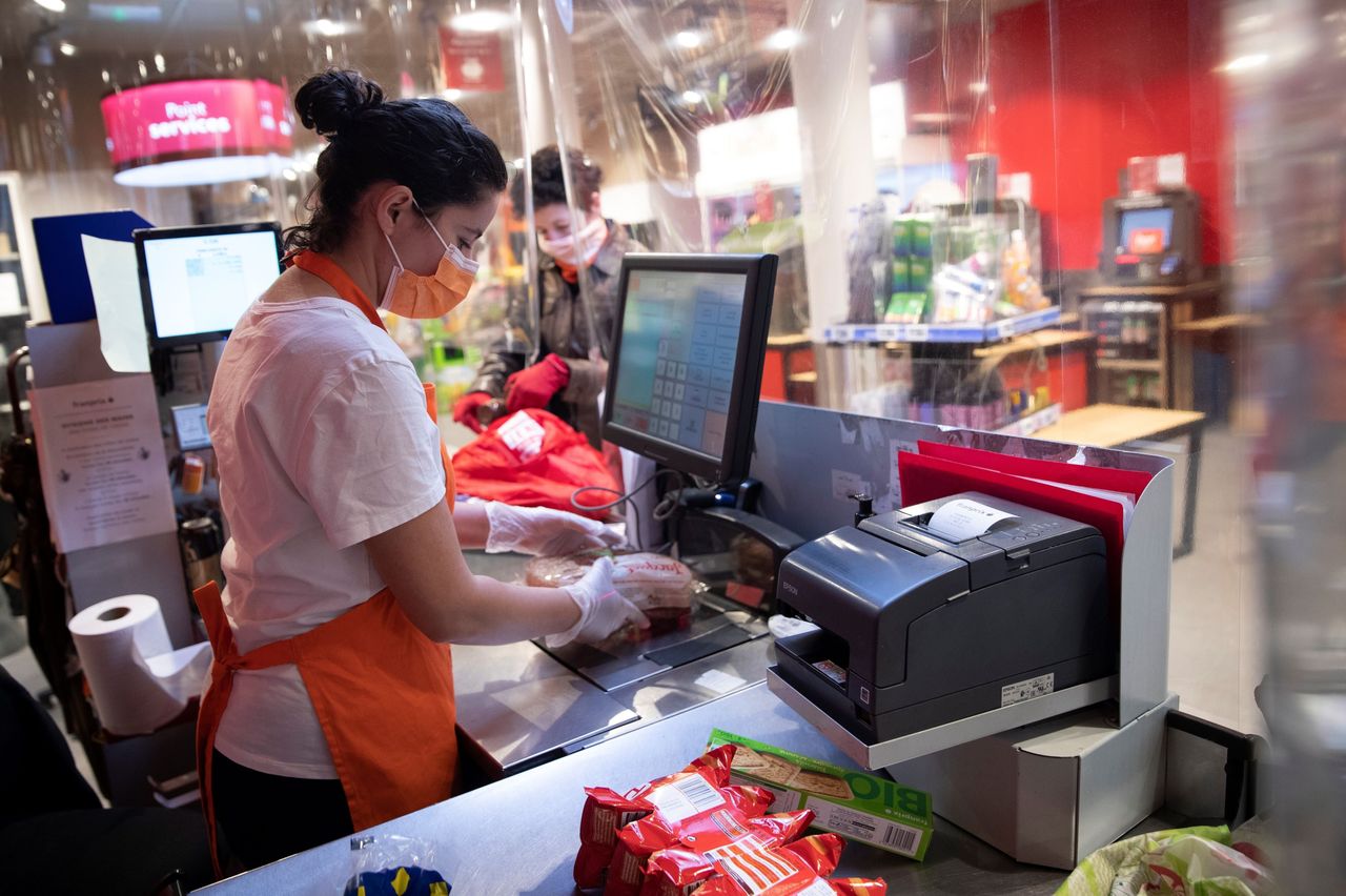 A cashier wearing a mask and gloves stands behind plastic sheeting at a supermarket in Paris on April 8. Such protective measures are likely to become more common as France and other countries lift lockdown restrictions.
