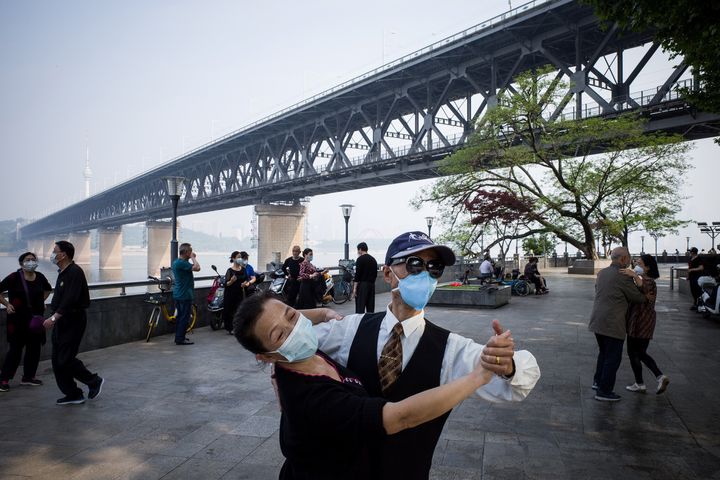 This photo taken on May 1, 2020 shows couples wearing face masks as a precaution against the COVID-19 coronavirus as they dance under Wuhan Bridge in Wuhan, in China's central Hubei province on the first day of the 5-day May Day national holiday. (Photo by STR / AFP) / China OUT (Photo by STR/AFP via Getty Images)