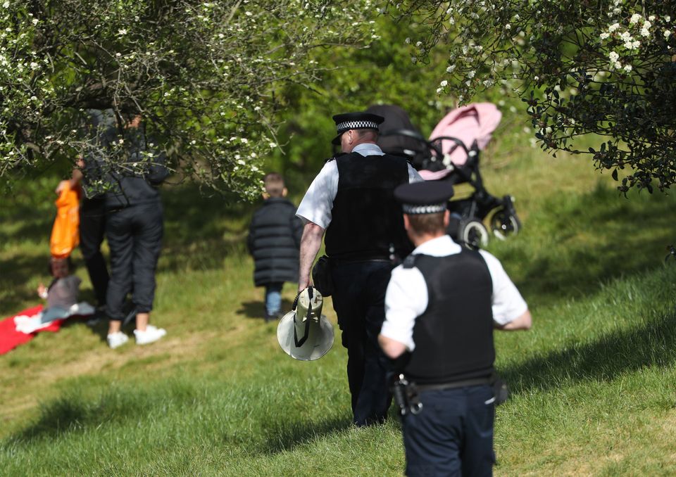 A police officer with a megaphone instructs people to keep moving in Greenwich Park, London.