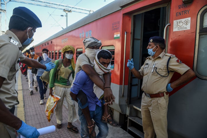 A migrant worker lifts his physically-challenged brother (C) as they arrive to board a special train to Agra in Uttar Pradesh, at Sabarmati Railway Station on the outskirts of Ahmedabad on May 2, 2020.