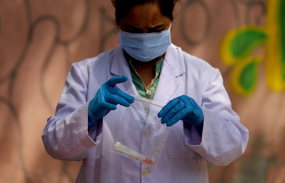 A medical worker wearing a protective suit seals a bag containing a swab sample 