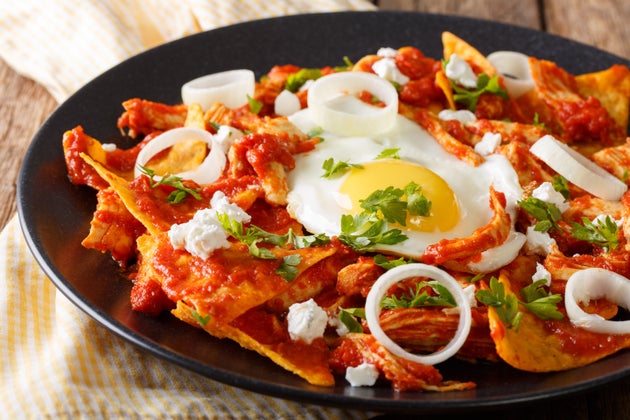 Tortillas with tomato salsa, chicken and egg close-up on a plate.