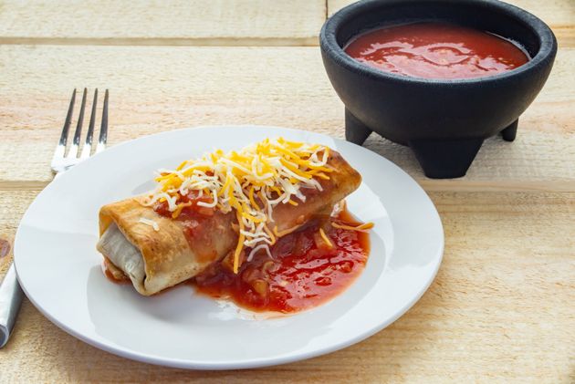A burrito on a plate covered in cheese and salsa