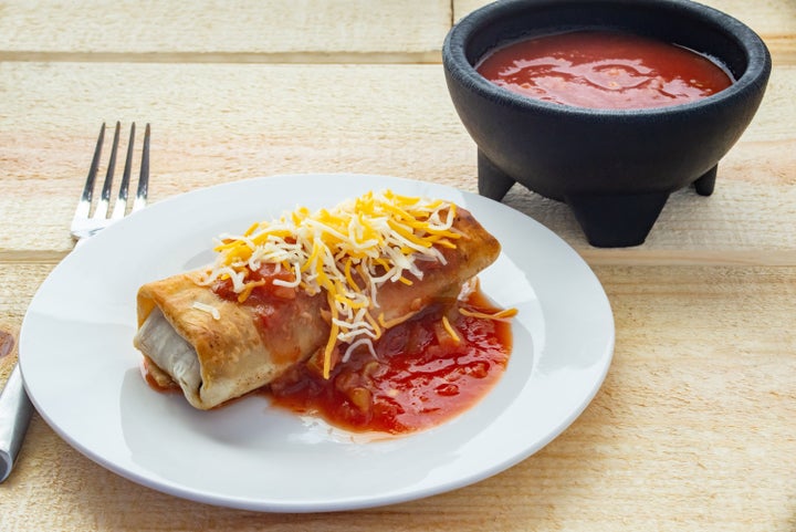 A burrito on a plate covered in cheese and salsa