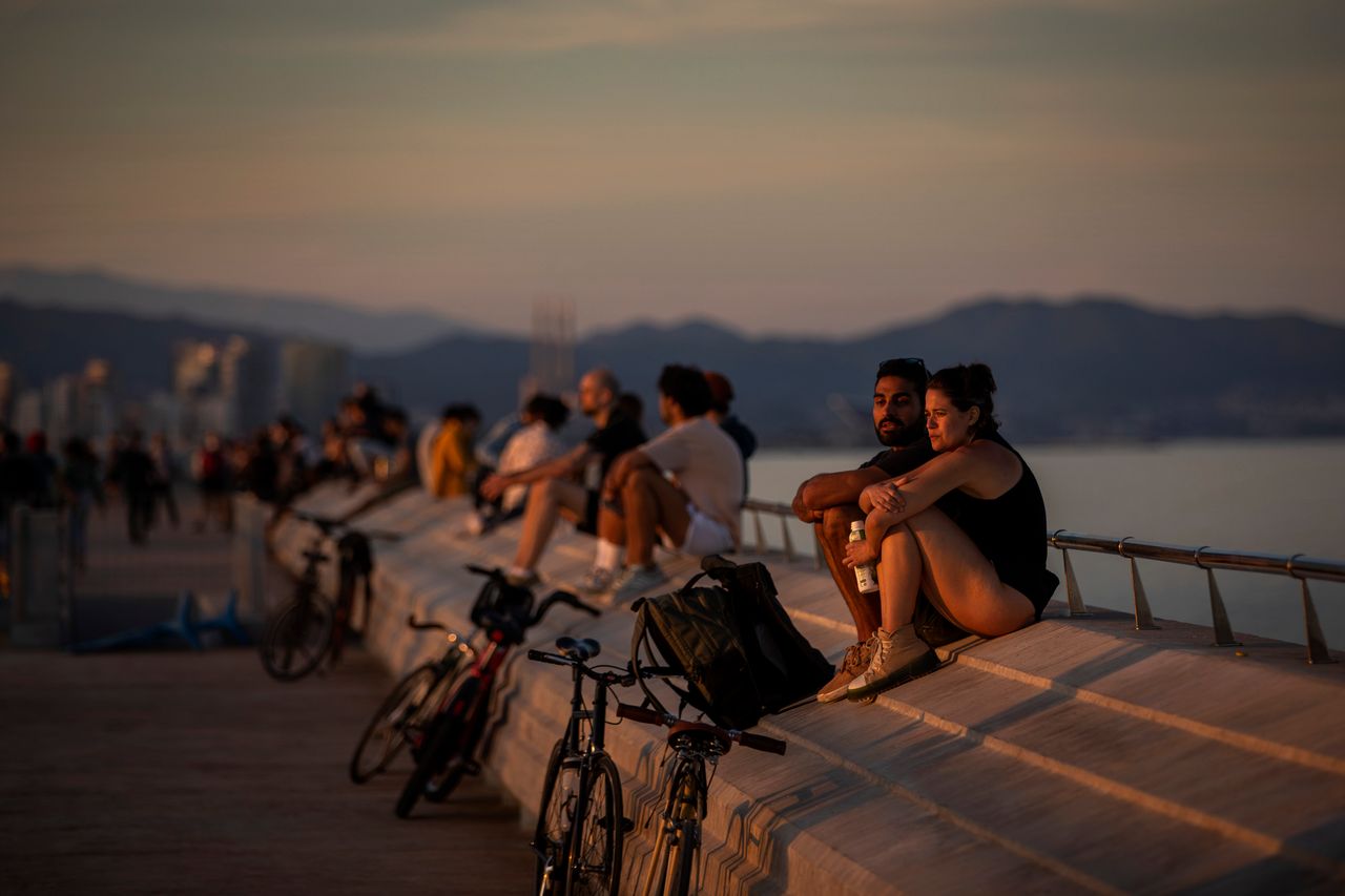 People sit on a seafront promenade during a sunset in Barcelona.
