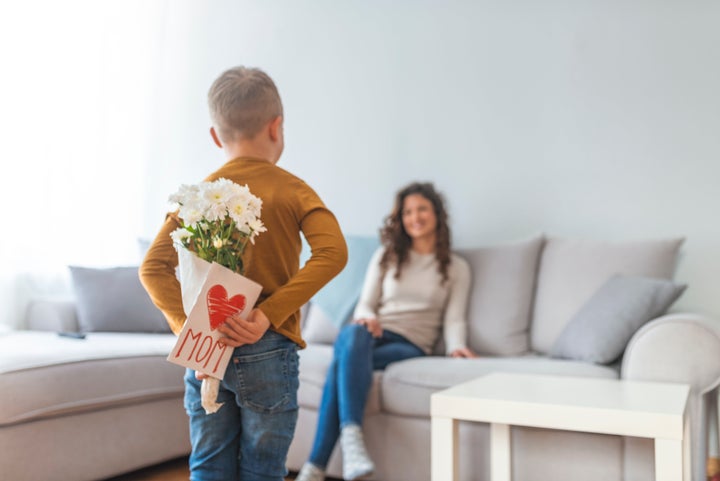 Happy mother's day! Child son congratulates moms and gives her a postcard. Child boy congratulates mother and gives a bouquet of flowers and gift