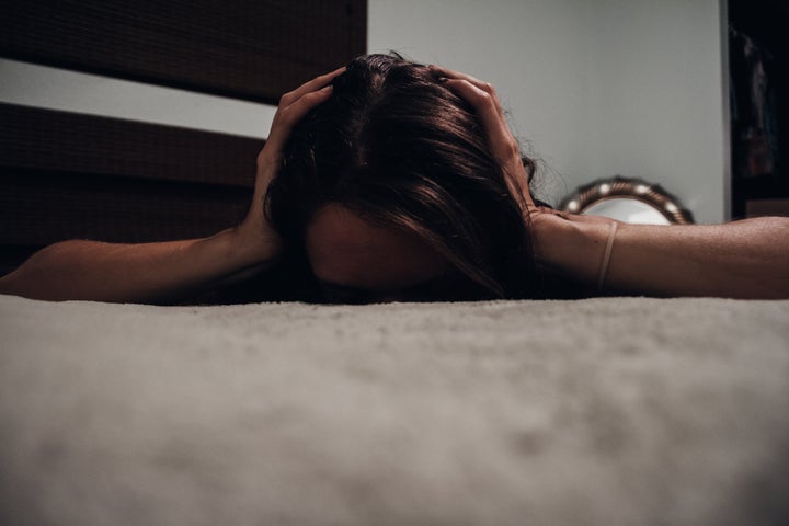 Young woman lying on bed face down with ears covered