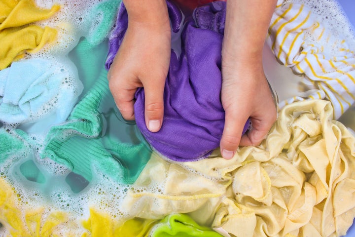 Female hands wash colored clothes in basin.