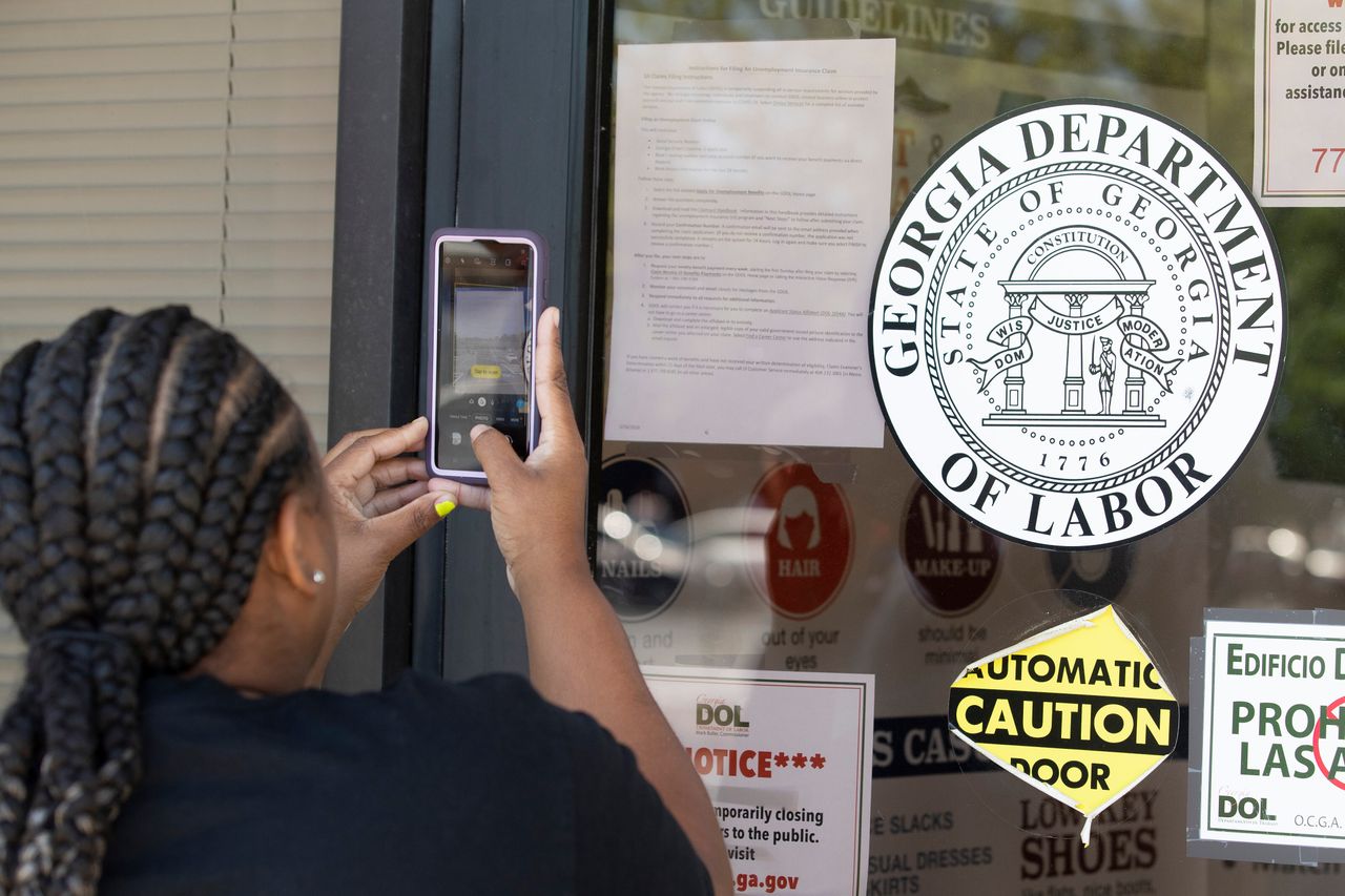 Arnashia McCain uses her phone to copy phone numbers posted on the locked doors of a Georgia Department of Labor office, May 7 in Norcross, Georgia. McCain, who said she drives for Lyft and has had her hours cut in her job in retail, has been unable check on the status of her her unemployment claim.