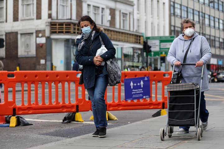 Two women wearing protective face coverings walk beside the recently widened pavement on Camden High Street in central London on Monday