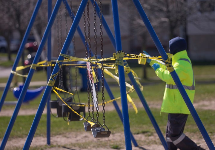 A City of Toronto employee reinstalls caution tape that was torn off a swing set on April 27, 2020.