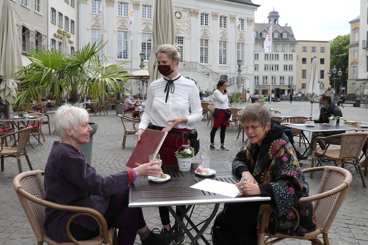 A waitress at Miebachs restaurant in Cologne, Germany, serves guests on May 12, 2020, the day after restaurants and cafes were allowed to reopen for the first time since March. The effort is part of a careful easing of restrictions as German authorities seek to raise economic activity while still monitoring the rates of coronavirus infection.