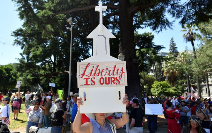 A woman help up a sign depicting a church as hundreds of people gathered earlier this month to protest the stay-at-home orders outside the state Capitol building in Sacramento. 