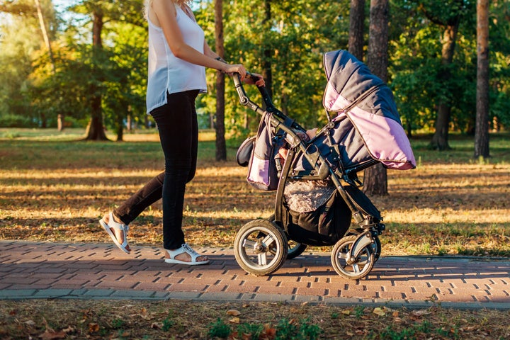 Mother's day. Young woman walking in spring park with baby carriage. Mother spends time with her toddler kid outdoors