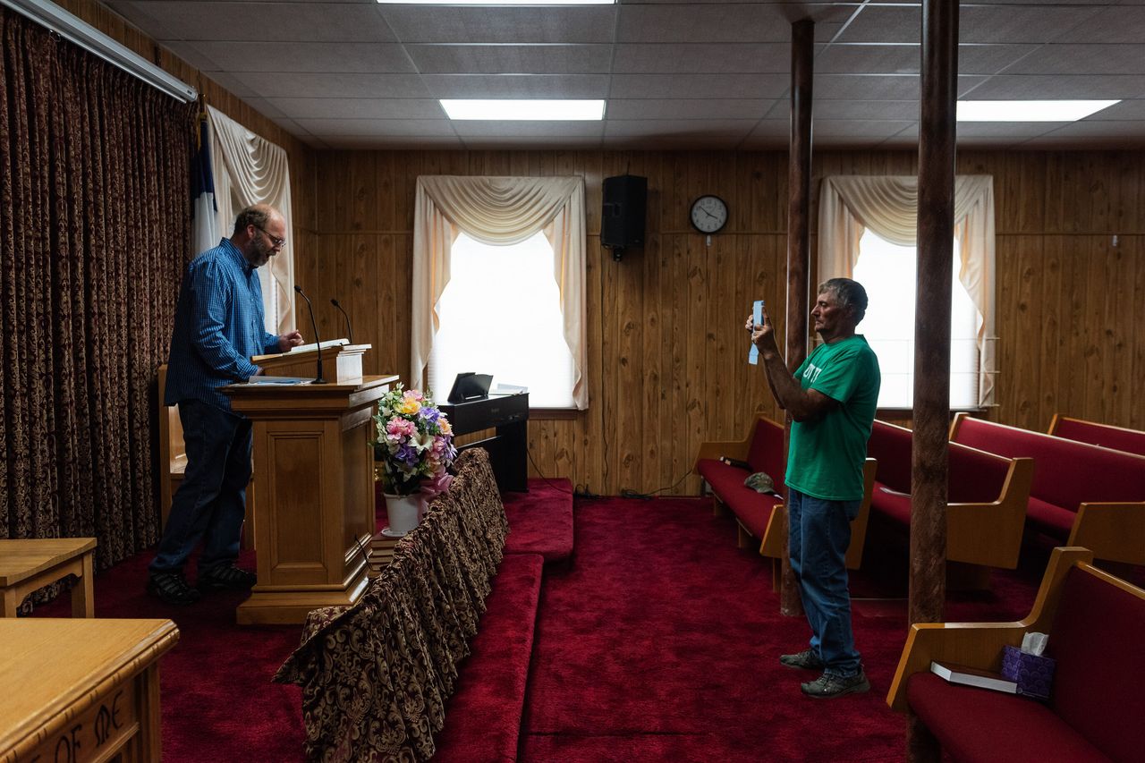 Tangier Mayor James "Ooker" Eskridge records a sermon by Duane Crockett, an elder of New Testament Congregation, inside the church to share on social media in lieu of regular service as a precaution against the spread of COVID-19 on the island.