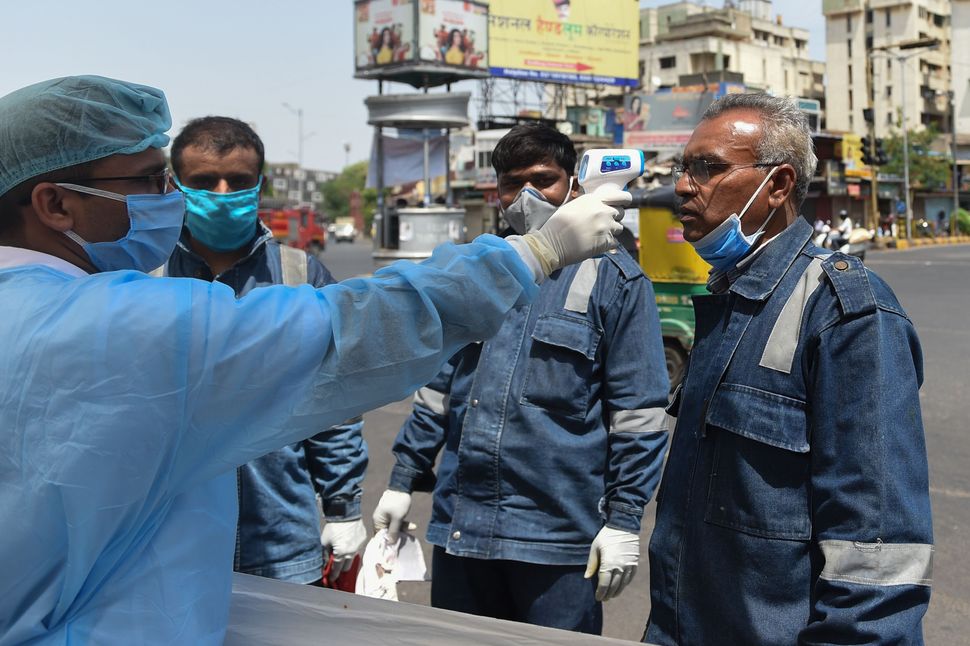 A health worker checks the body temperature of a Ahmedabad Fire & Emergency Services official during a nationwide lockdown as a preventive measure against the COVID-19 coronavirus in the Walled City region of Ahmedabad on April 8, 2020. 