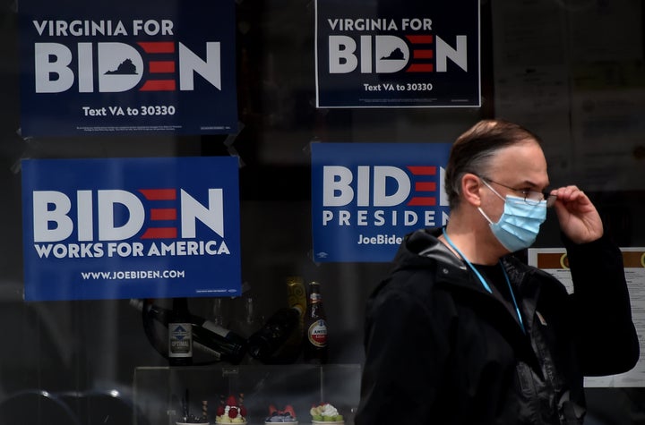 A man wearing a face mask walks past signs Monday in Alexandria, Virginia, for Joe Biden's 2020 presidential campaign amid the coronavirus outbreak.