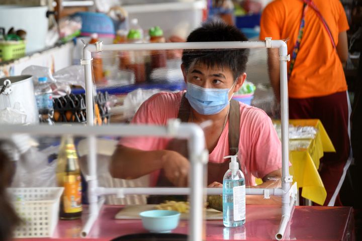 Ανδρας τρώει το μεσημεριανό του σε εστιατόριο street food, κρατώντας τις απαραίτητες αποστάσεις. Βρίσκεται πίσω από διαχωριστικό πλεξιγκλάς. Η κυβέρνηση της Ταϊλάνδης χαλάρωσε τα μέτρα, όμως οι αποστάσεις είναι σημαντικές. 