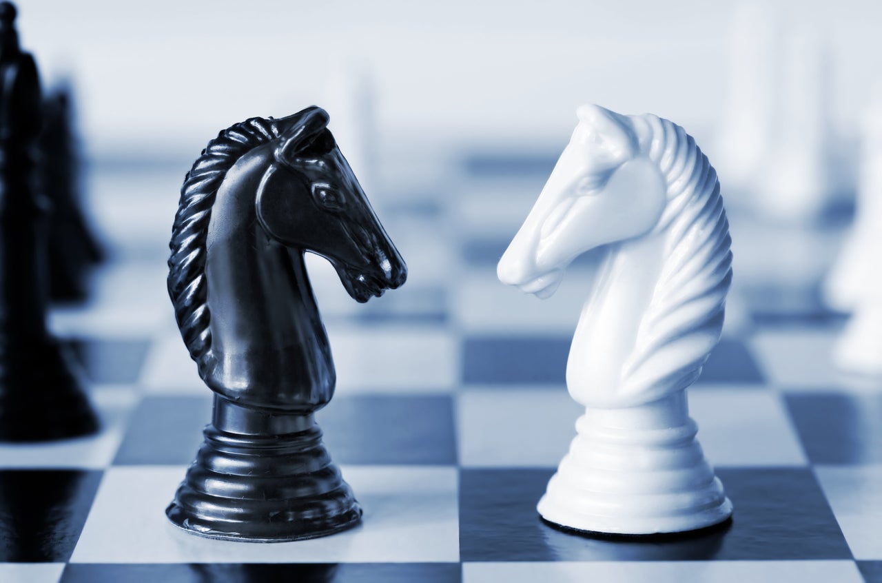 Head to head - knights on a chess board, in blue duotone. Shallow depth of field.