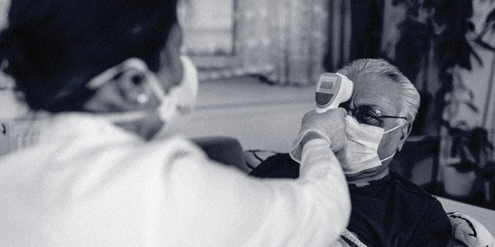 A health worker wearing personal protective equipment takes a person's temperature.