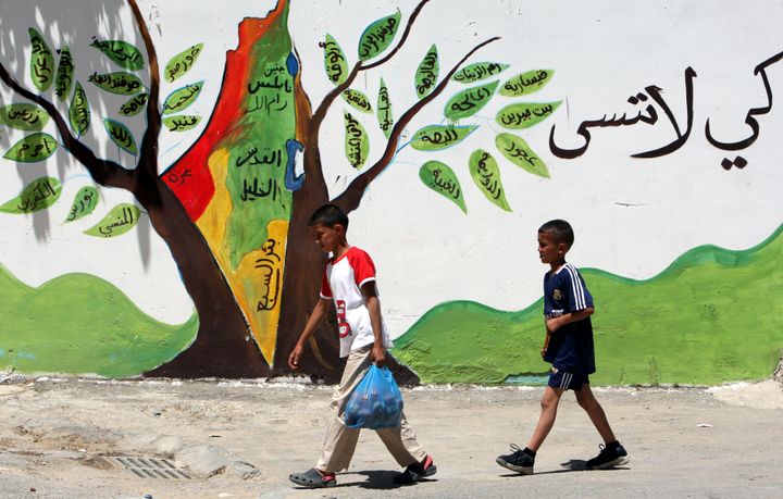 Νεαροί Παλαιστίνιοι περνούν μπροστά από ένα graffiti στο οποίο απεικονίζεται ένα δέντρο πάνω στο οποίο αναγράφονται τα ονόματα των χωριών και τονω πόλεων από τα οποία οι Παλαιστίνιοι εκδιώχθηκαν το 1948.AP Photo/Mohammed Ballas)