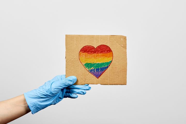 LGBTQ friendly healthcare system worker holding handmade placard with heart-shaped rainbow flag. LGBTQ doctor fighting on frontline against coronavirus