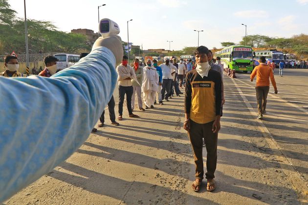 Migrants undergo thermal screening before boarding buses to their native places,during the ongoing COVID-19...