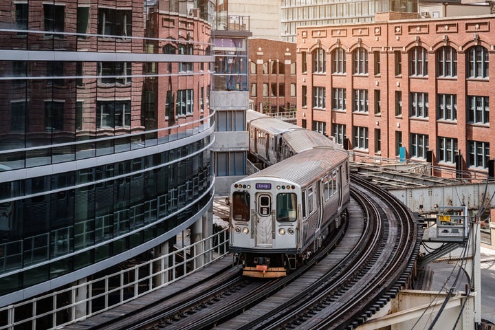 A commuter train moving on elevated tracks between buildings in Chicago. The New York Times calls public transit "an infrastructure of opportunity."