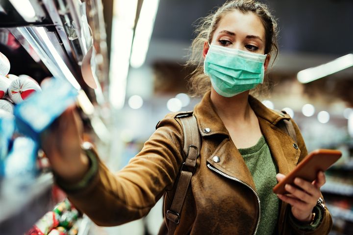 In this stock photo, a woman in a face mask checks the price on an item in a supermarket. Canadians are seeing rising food prices in the pandemic, even as deflation hits the broader economy.