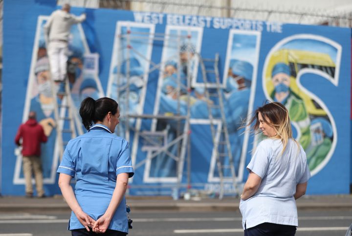 Nurses watch as a mural is painted in recognition of the NHS on the Falls Road in Belfast, as the UK continues in lockdown to help curb the spread of the coronavirus