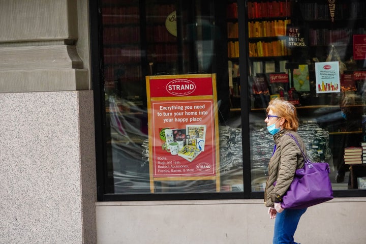 A pedestrian passes the closed doors of The Strand, an indie bookstore in New York City. A sign in the window advertises "everything you need to turn your home into your happy place."