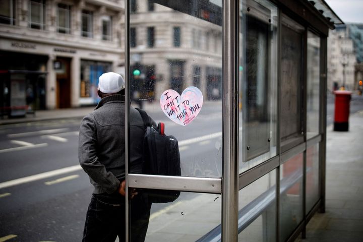 A sticker reading "I can't wait to hug you" is pictured as a man waits at a bus stop in central London.