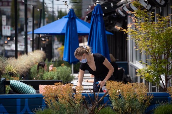 A server wears a face mask while cleaning a table on the patio at an Earls restaurant in Vancouver on May 19, 2020.
