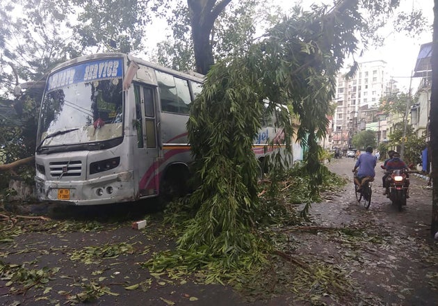 Commuters in Kolkata move past a tree branch precariously hanging over a bus after cyclone Amphan hit...