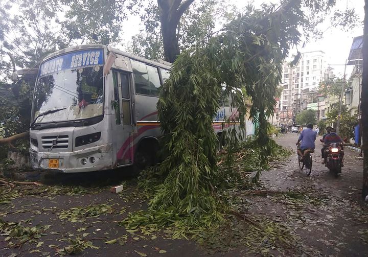 Commuters in Kolkata move past a tree branch precariously hanging over a bus after cyclone Amphan hit the region on May 21, 2020. 